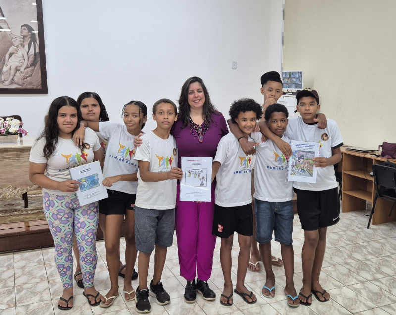 A group of seven boys and two girls from the Moleques do Bem project stand proudly with project leader Raquel Pádua, holding up their illustrated books and creative work