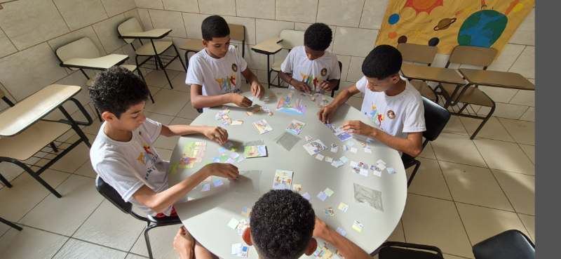 Five boys sit around a classroom table working on colorful puzzle pieces and drawings as part of a creative workshop