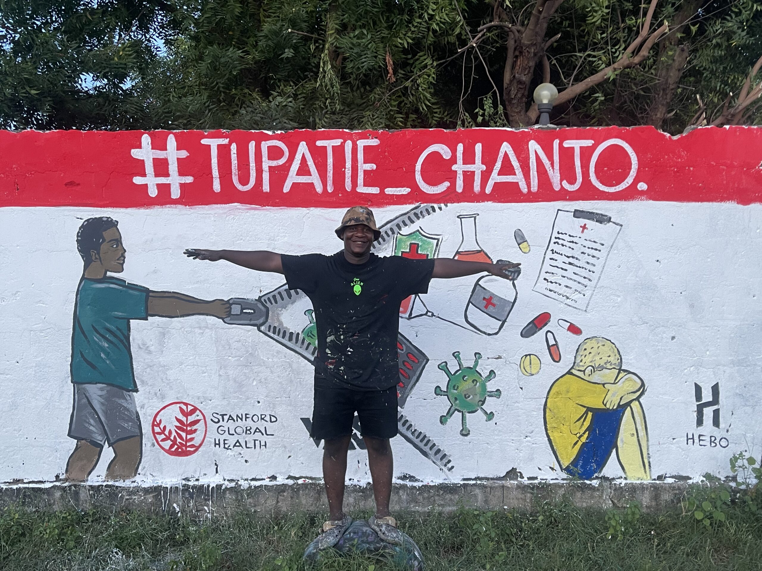 An artist in front a mural with arms open