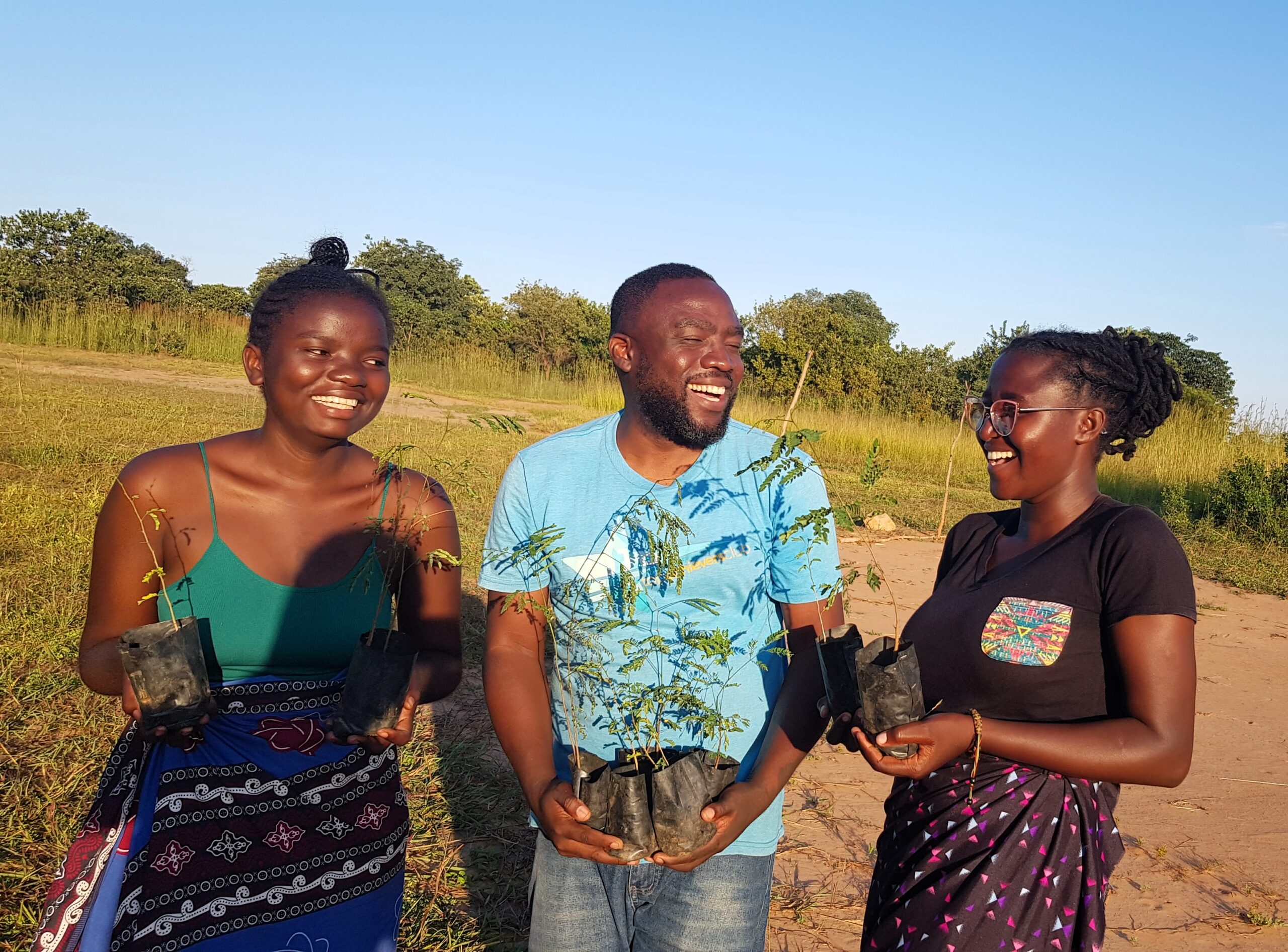 Two young women and a man smiling and holding little trees ready to be planted